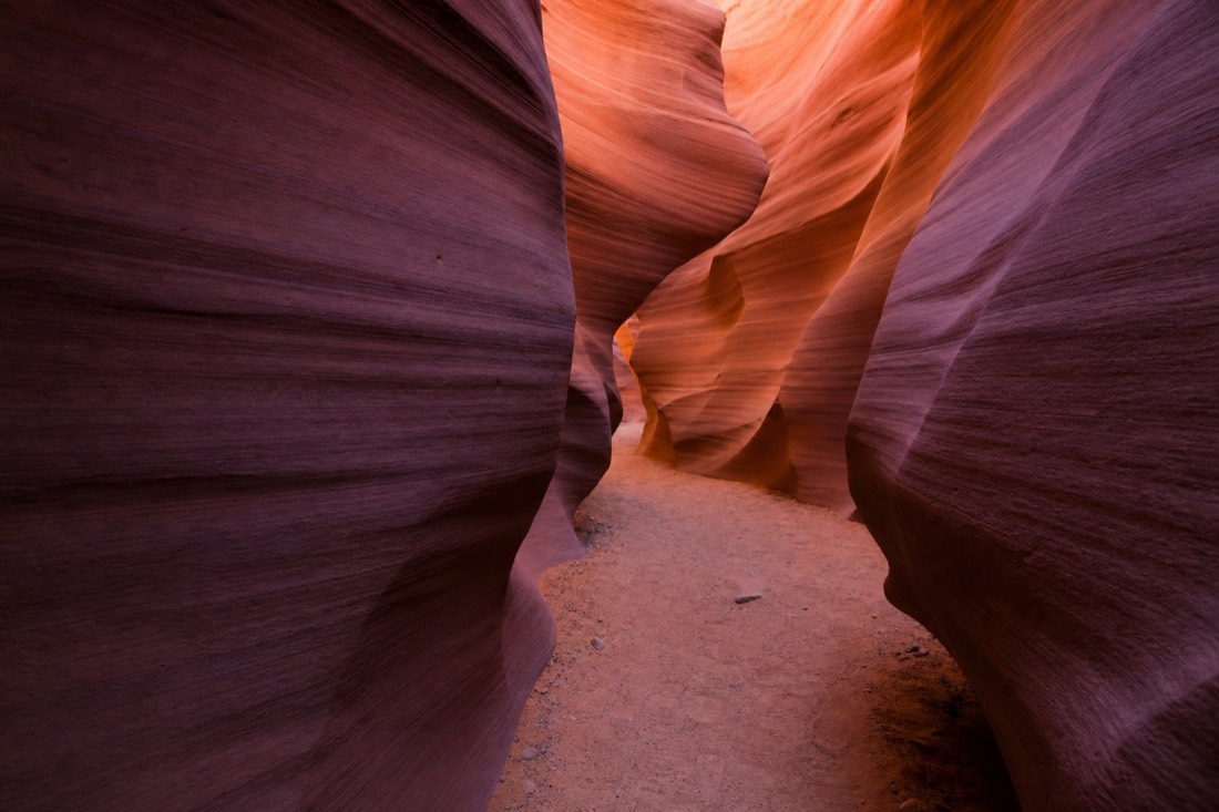 Visitors walking the wide sandy floor of Upper Antelope Canyon beneath curved orange sandstone